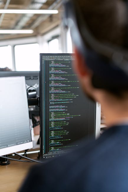 A modern silver laptop with a black keyboard is positioned on a light wooden table, displaying lines of programming code with syntax highlighting on its screen. The laptop's display appears bright and