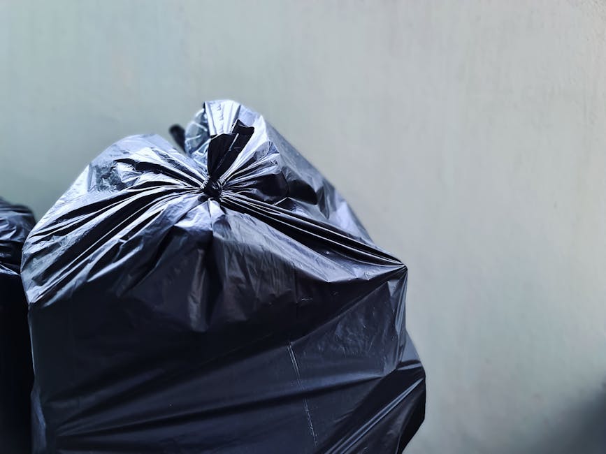 A collection of multiple large white plastic rubbish bags filled with waste, each tightly knotted at the top with orange plastic ties, placed outdoors on a paved surface. The bags appear to be full an